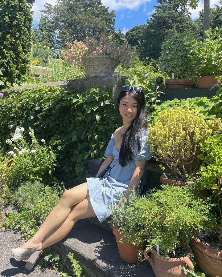 Claire Liu Yang sitting on stone garden steps among flowers and potted plants